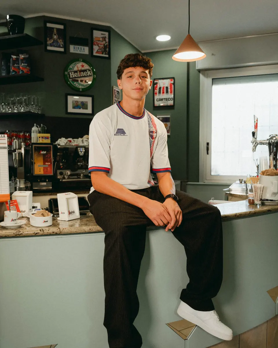 Un ragazzo con la maglia bianca 2026/27 dell’Imolese seduto sul bancone di un bar