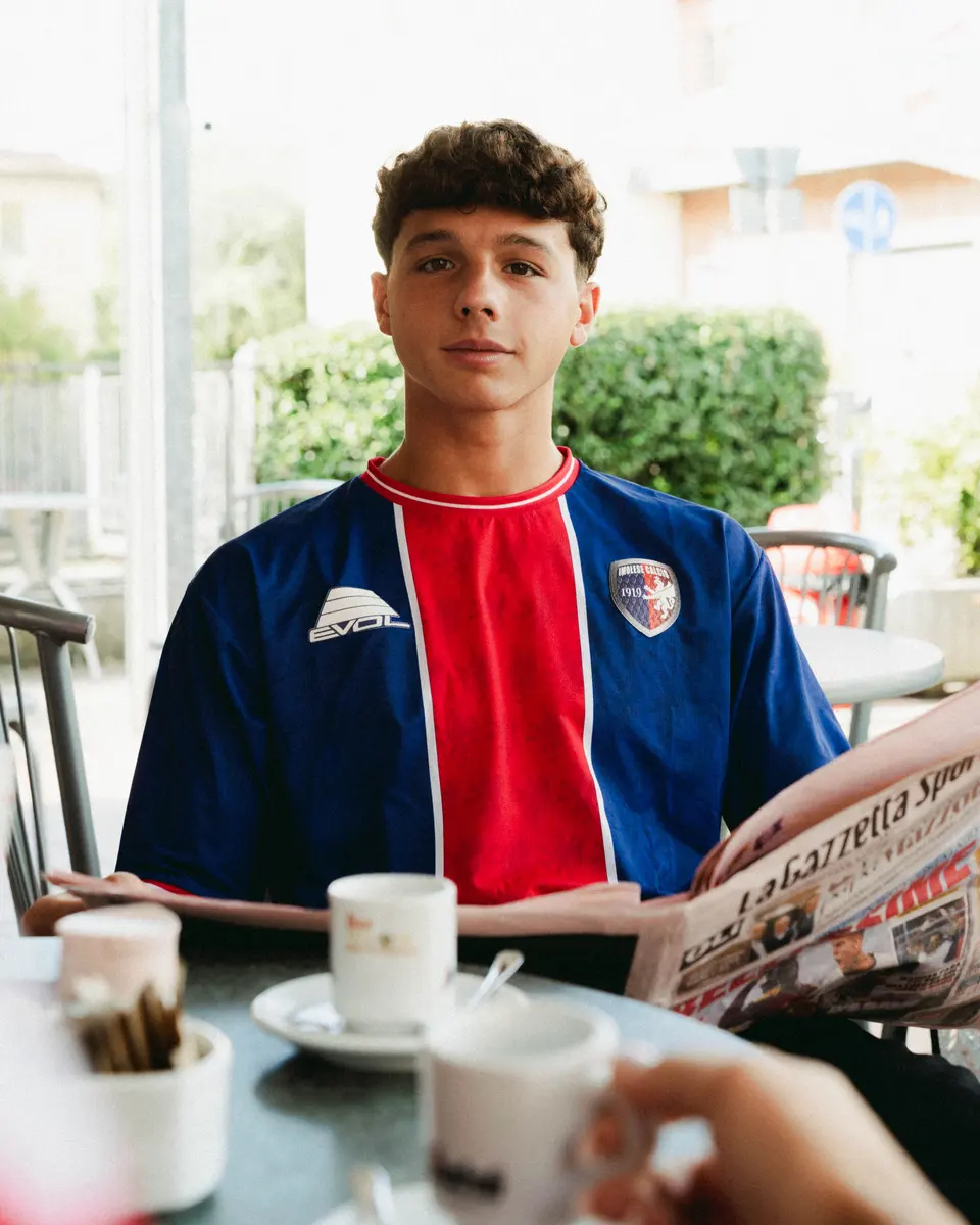 Un ragazzo con la maglia blu e rossa 2026/27 dell’Imolese al tavolino del bar con il giornale sportivo