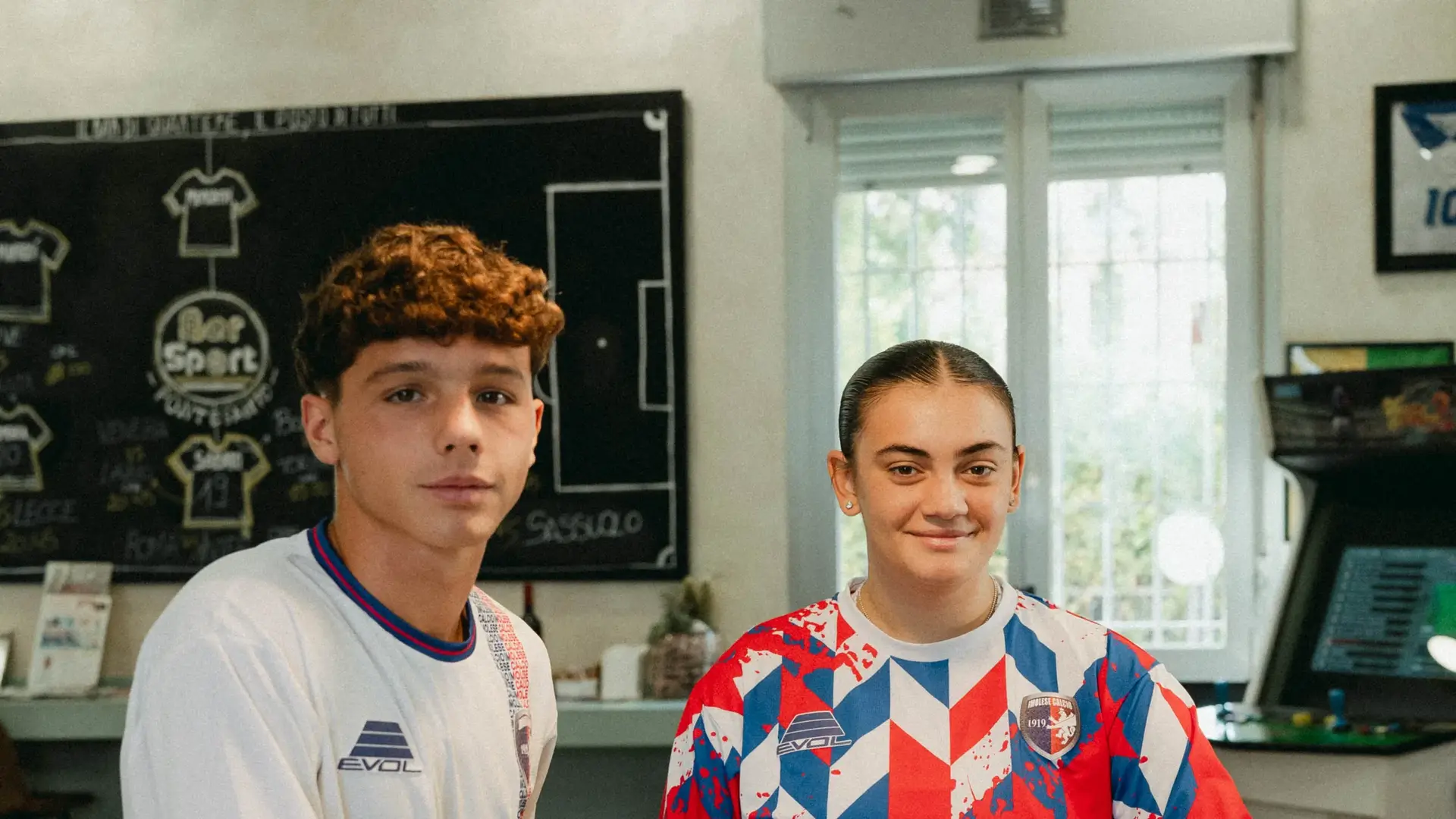 Due ragazzi con le maglie 2026/27 dell’Imolese al bancone del bar sotto la lavagna del Bar Sport